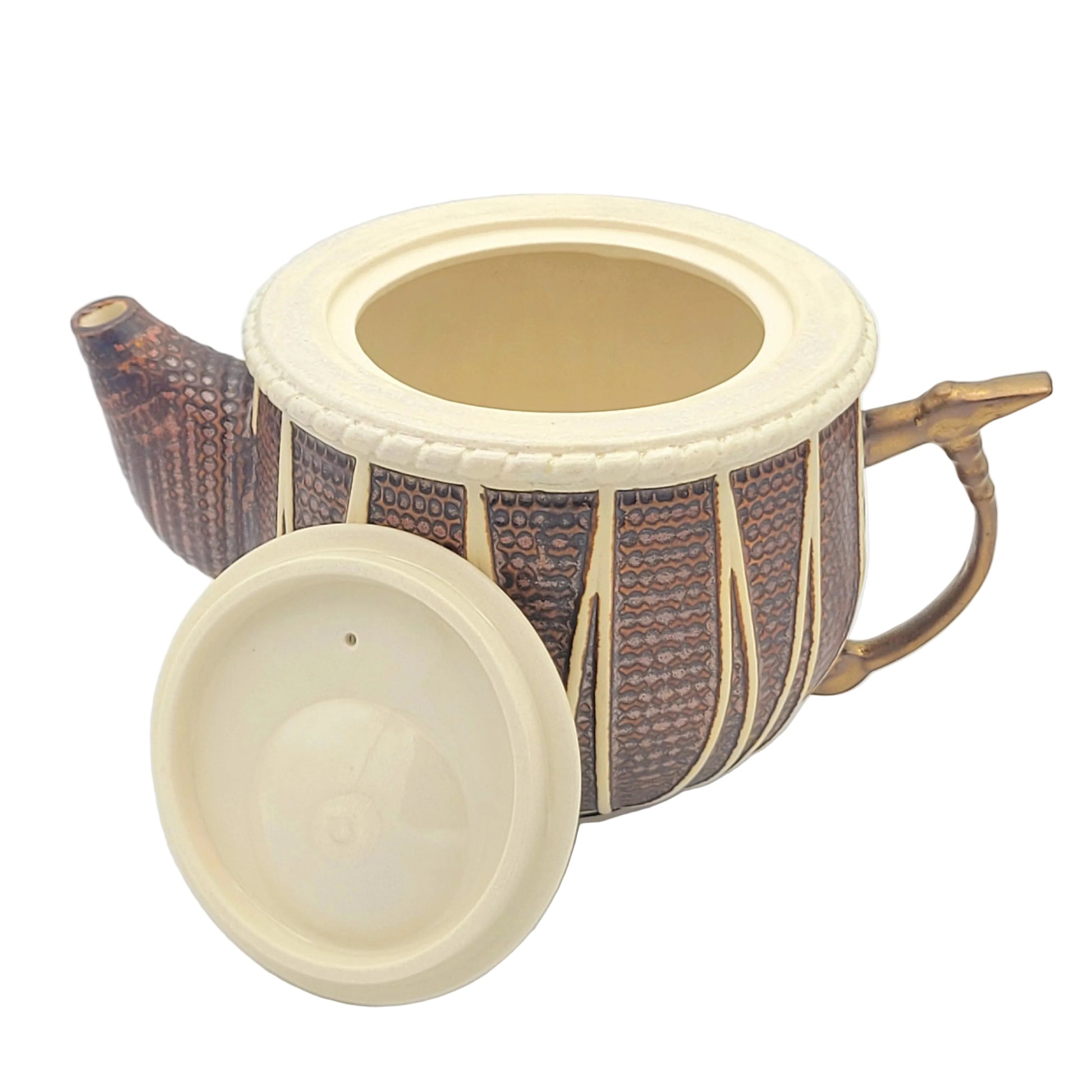 A decorative ceramic teapot with a copper colored glazed body, cream-colored rim and lid, and a gold-toned tabla hammer handle, shown on a white background