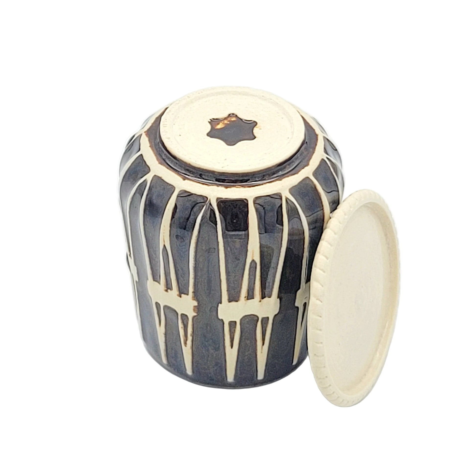 A small handcrafted ceramic drum with a glossy black body, cream-colored vertical stripes, a cream-colored top, and a matching cream-colored lid leaning against it, set against a plain white background.